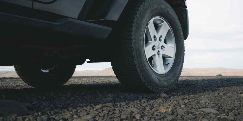 The image shows a close-up of a vehicle's tire on rough, rocky terrain, likely depicting off-road capability.