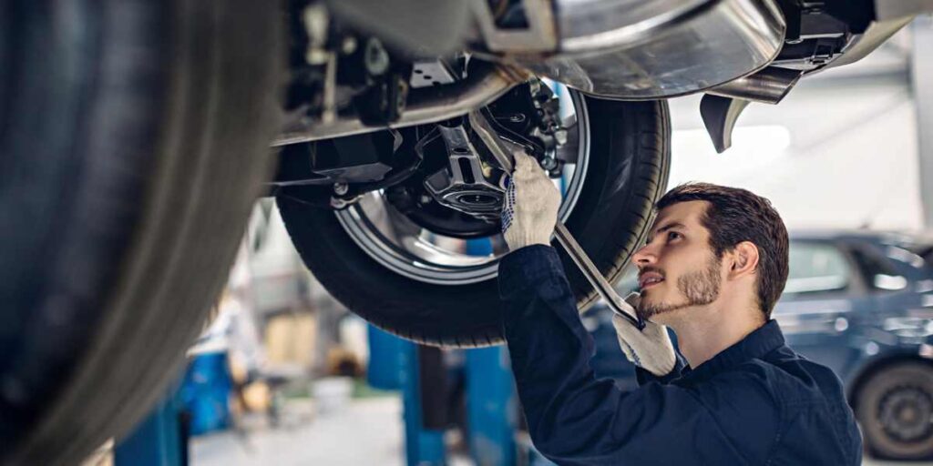 A mechanic is working underneath a vehicle, inspecting or repairing the car's suspension or exhaust system.