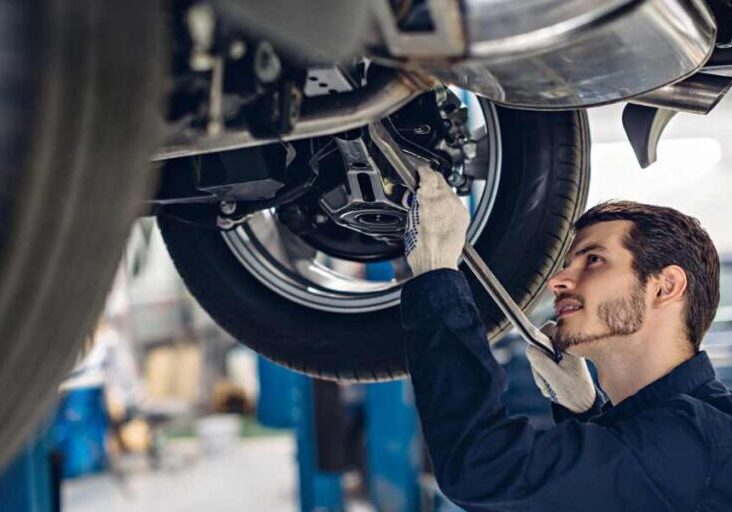 A mechanic is working underneath a vehicle, inspecting or repairing the car's suspension or exhaust system.