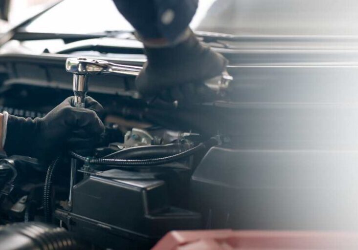 A mechanic wearing gloves is working on a car engine with a wrench.