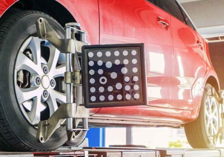 A red car undergoing a wheel alignment check with measuring equipment attached to the rims.